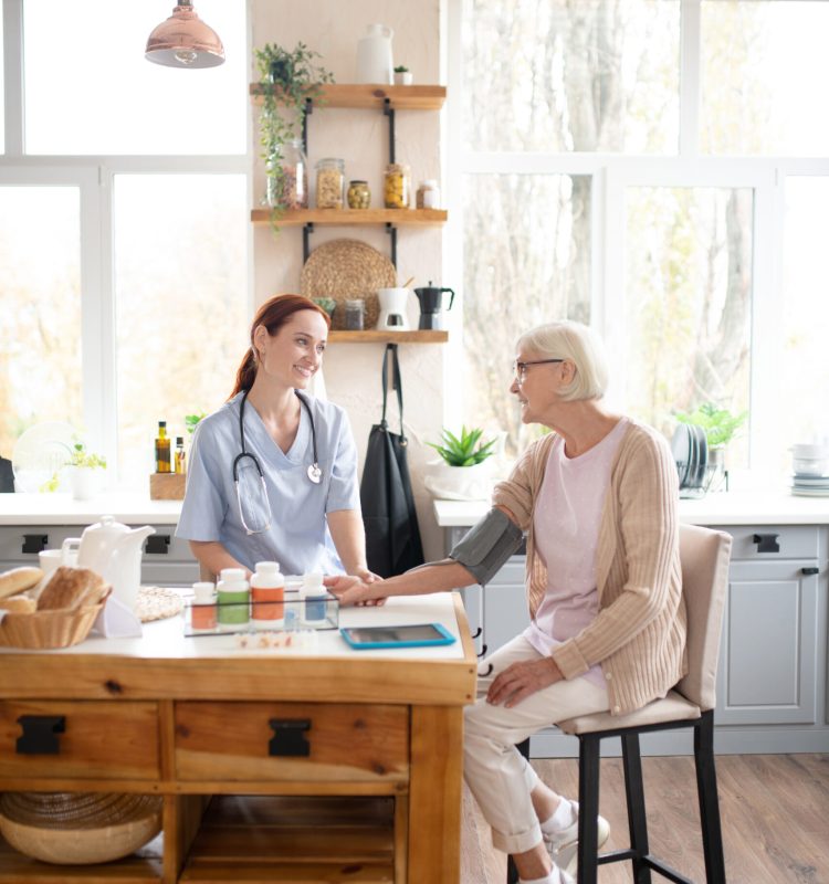 Visiting aged lady. Kind professional nurse visiting aged lady measuring pressure and speaking